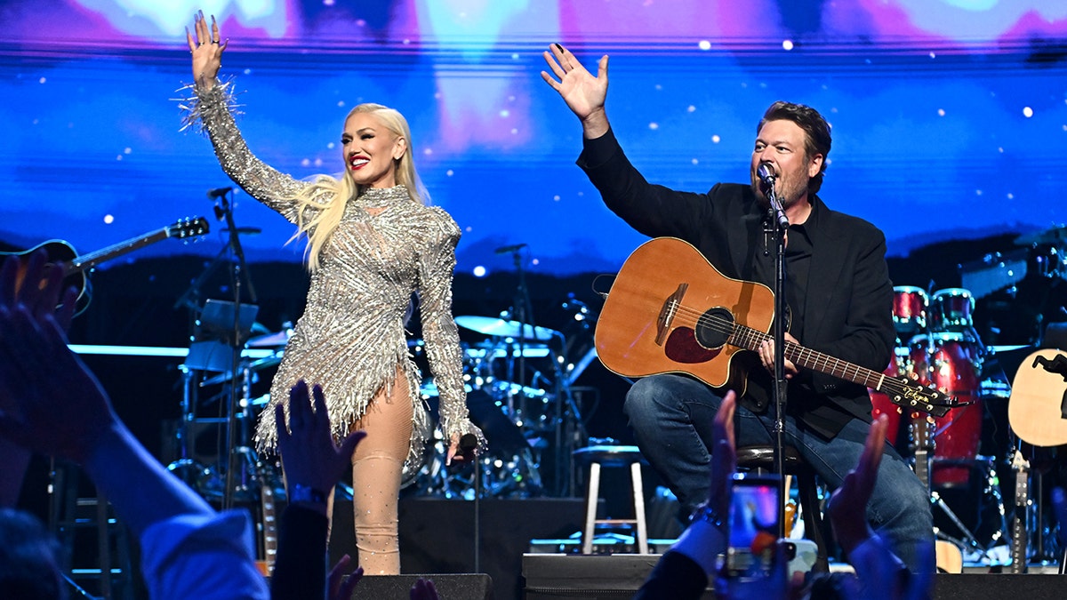 Gwen Stefani, con un vestido plateado brillante, saluda al público en sincronía con su marido Blake Shelton, sentado en un taburete con su guitarra, en la Gala Power of Love.