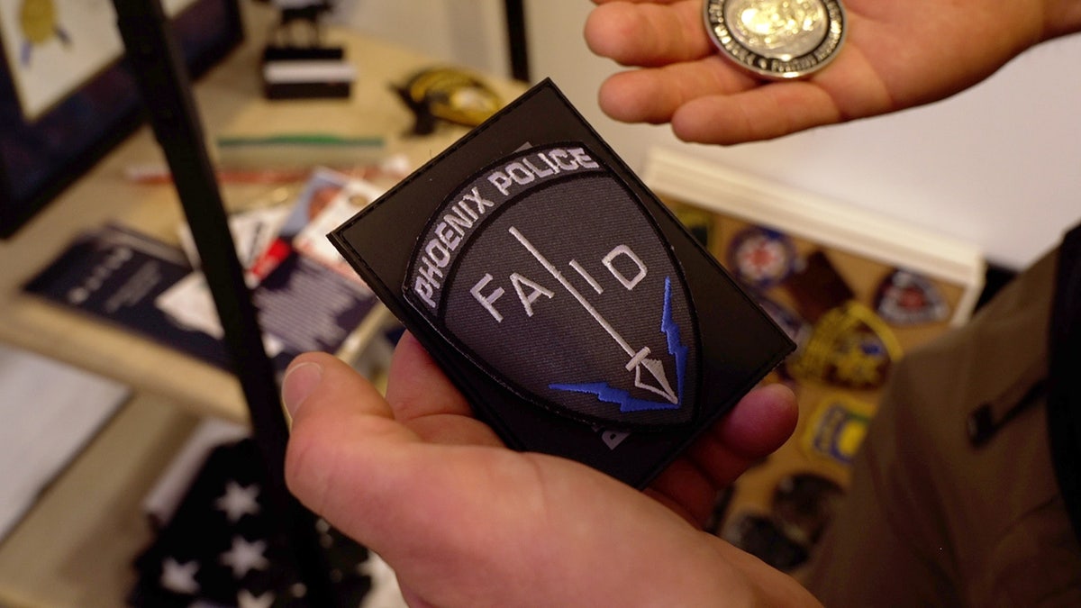 Hands hold Phoenix Police patch and a challenge coin