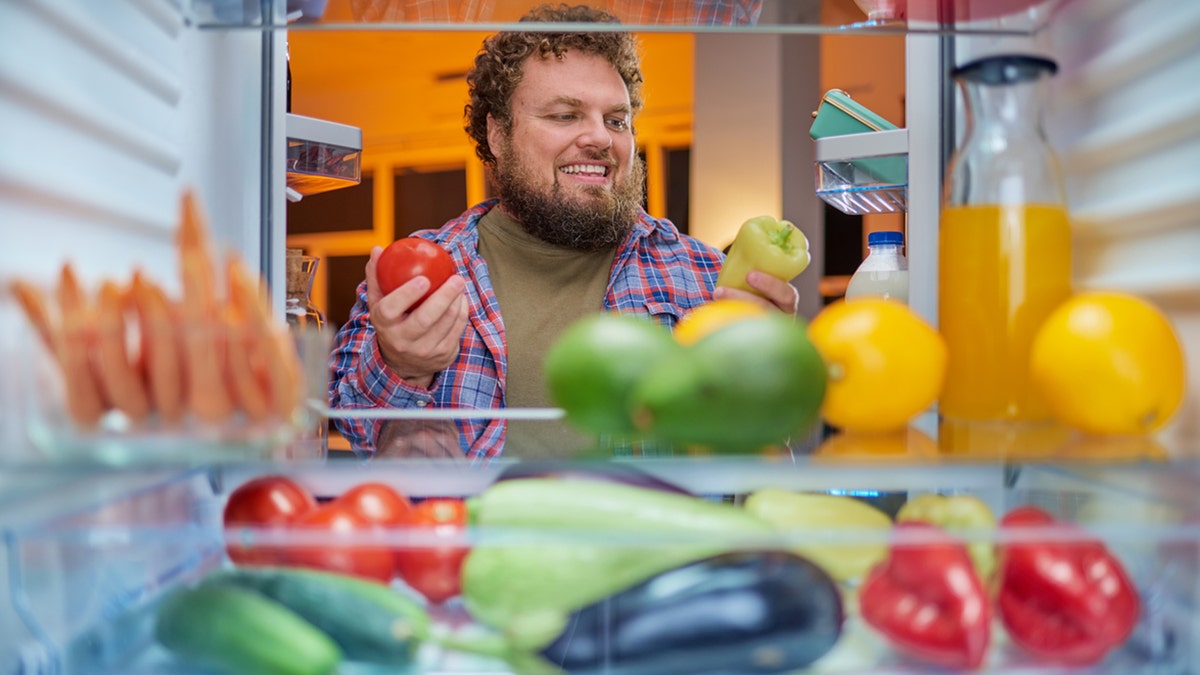 man picks fruits and veggies out of the fridge