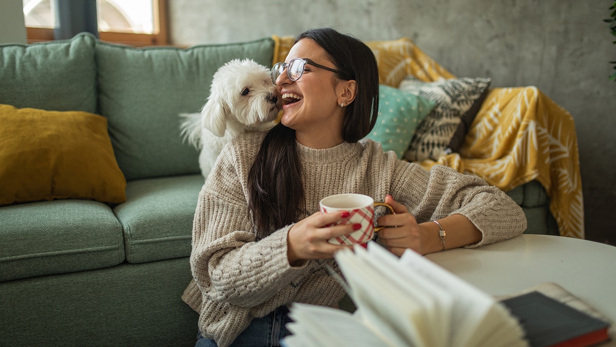 woman kisses her dog while drinking tea