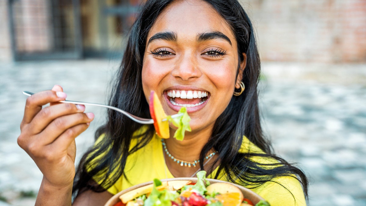 Mujer sonríe mientras come una ensalada