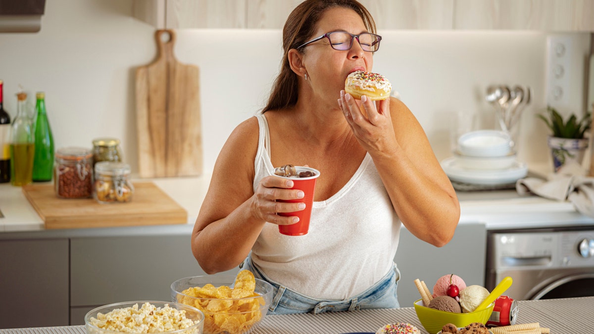 Woman eating a doughnut and drinking soda in her kitchen