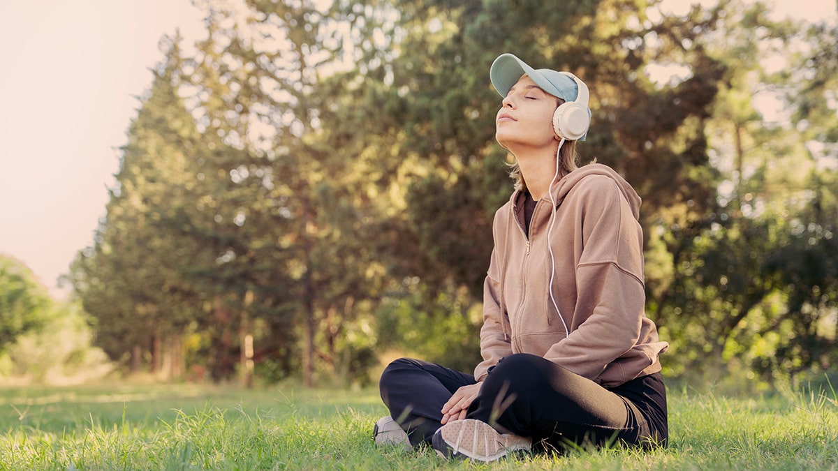 woman meditates outside with headphones on