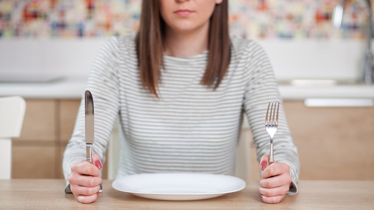 woman sits in front of an empty plate.