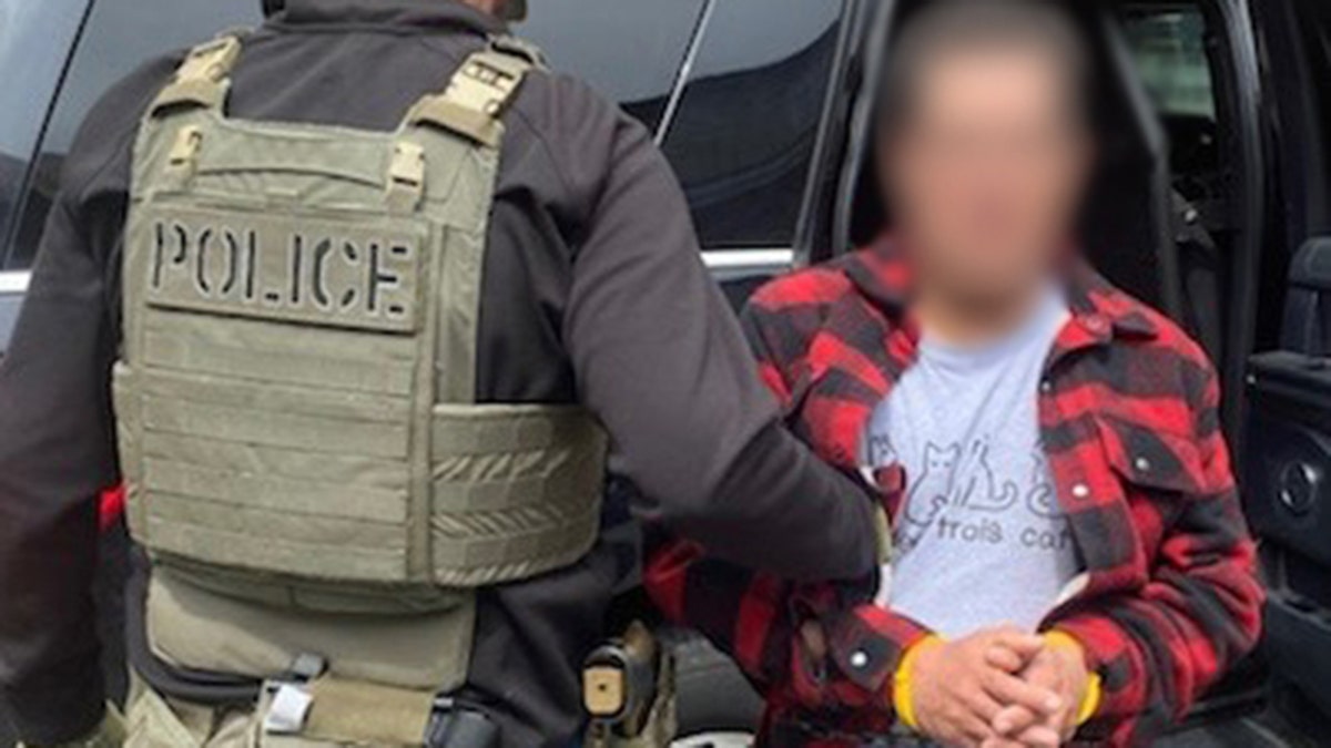 ICE office in green "police" vest with Colombian national being arrested, his face blurred