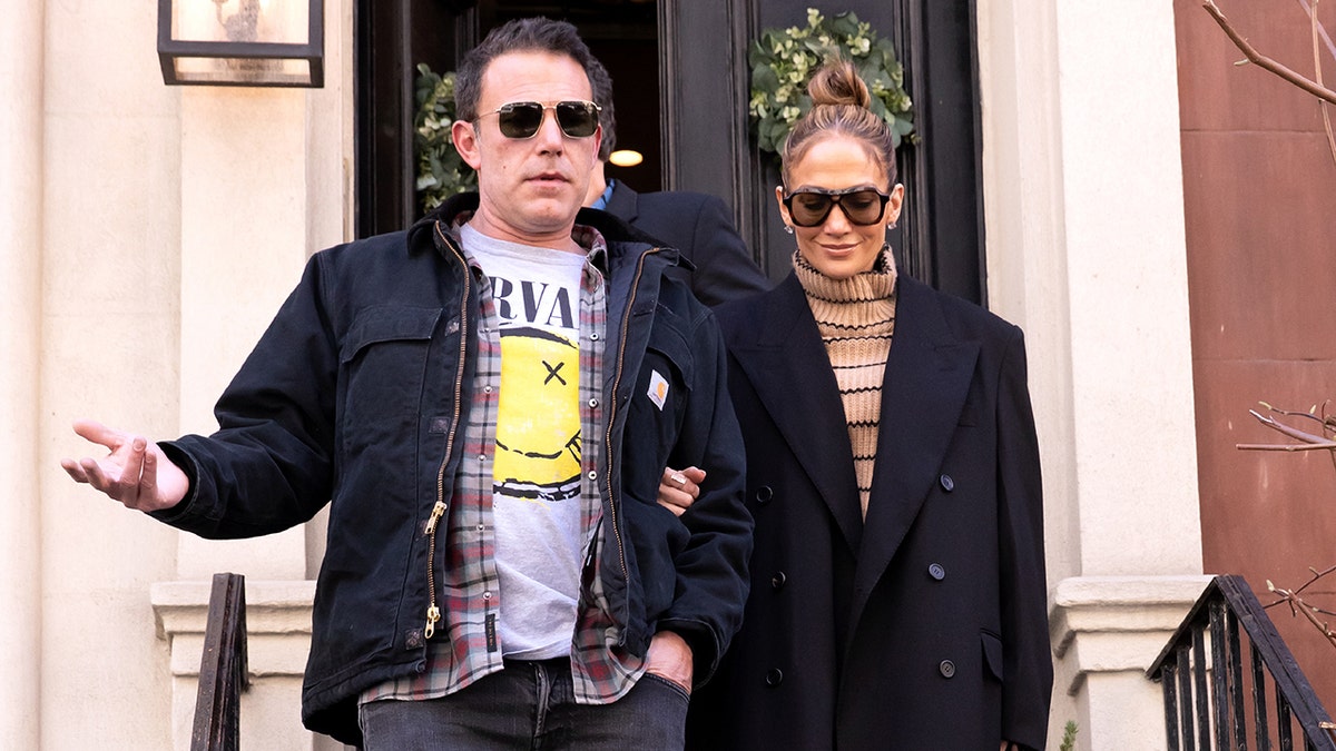 Ben Affleck in a Nirvana t-shirt and jacket walks down New York stairs with wife Jennifer Lopez in a large peacoat