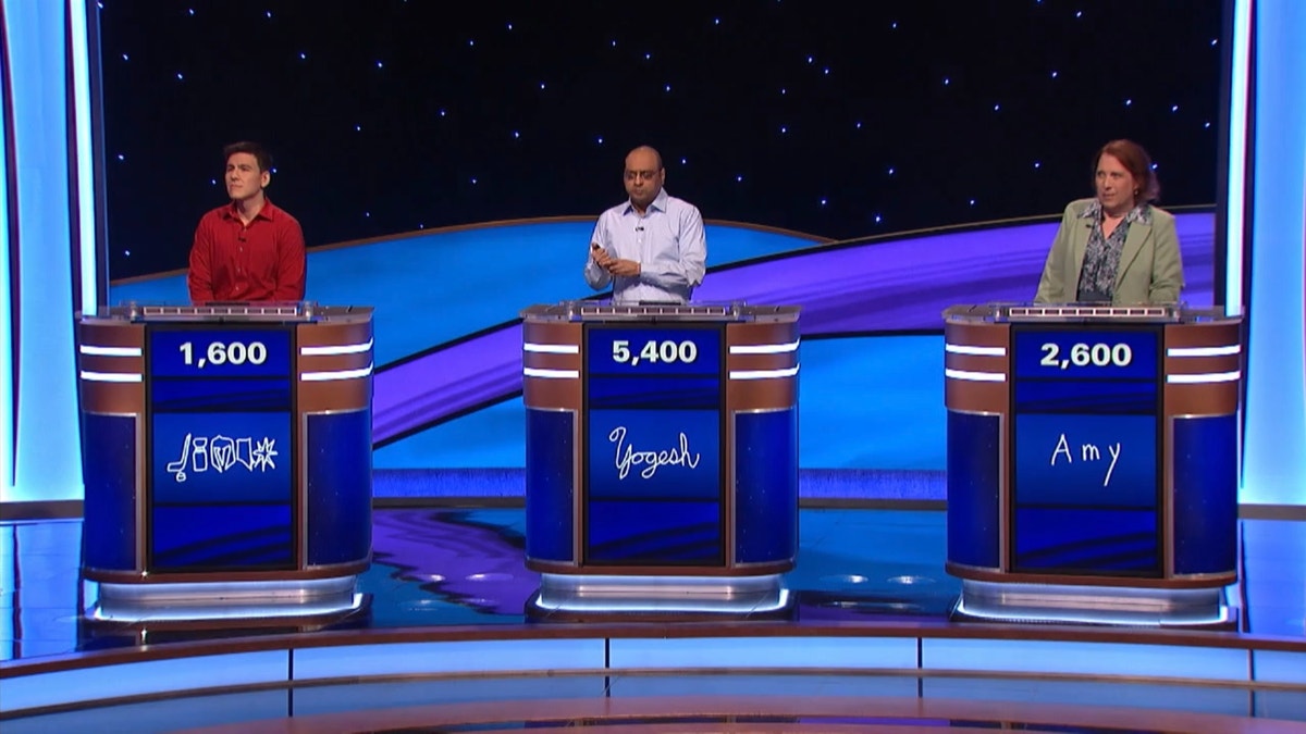 James Holzhauer in red, Yogesh Raut in light blue and Amy Schneider in a green blazer stand behind the podiums during "Jeopardy! Masters"