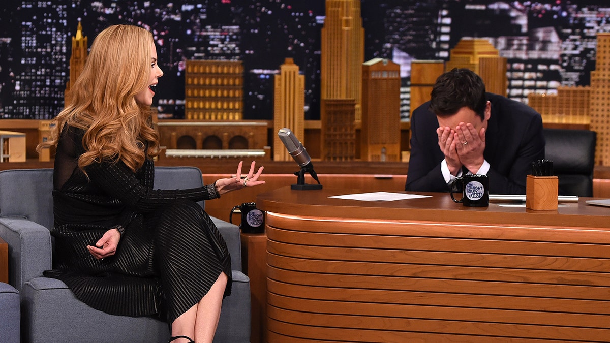 Jimmy Fallon covers his face with his hands as he sits across from Nicole Kidman in a black dress during "The Tonight Show"