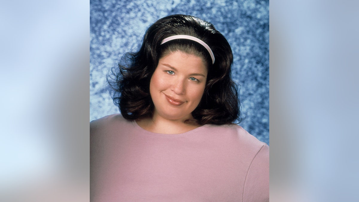 Lori Beth Denberg in a headshot from the Steve Harvey Show in a mauve sweater and headband