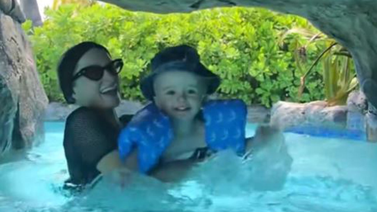 Paris Hilton covers up in black swimsuit while in the pool with her son.