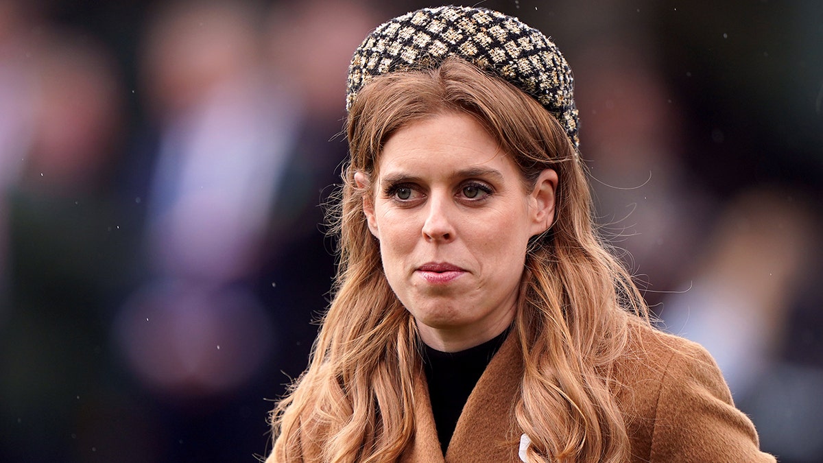 Princess Beatrice in a checkered round hat that sits upon her head and a camel colored coat 