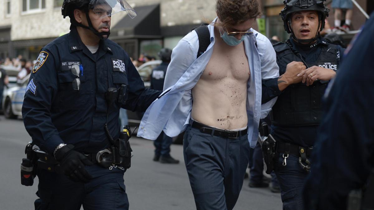 A man with an open shirt is arrested by police