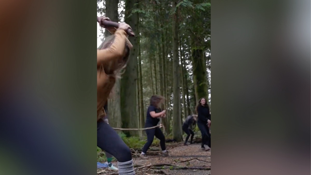 women hitting ground with sticks in a forest