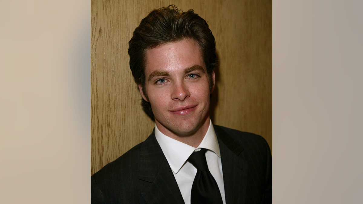 A young Chris Pine soft smiles in a dark suit and tie