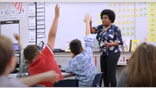 Students raising hands in front of teacher