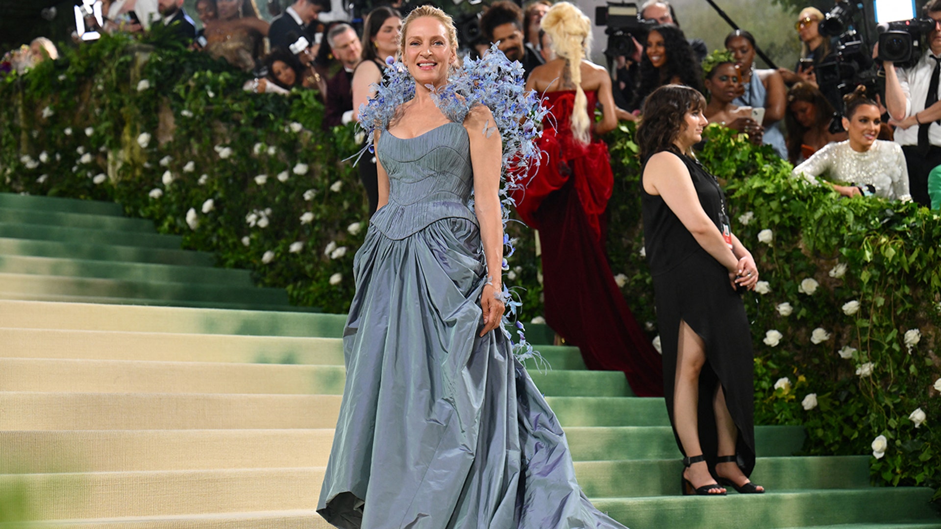 Uma Thurman at the Met Gala 2024 red carpet in a blue Tori Burch gown with butterflies on the shoulders.