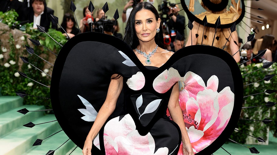 Demi Moore at the Met Gala 2024 red carpet, wearing a black dress with floral print designed by Harris Reed.