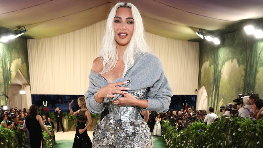 Kim Kardashian at the Met Gala 2024 red carpet in a corseted sheer Margiela by John Galliano dress, with a lace train and floral accents.