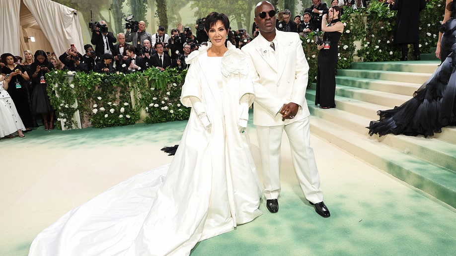 Kris Jenner at the Met Gala 2024 red carpet in a white satin gown and overcoat designed by Oscar de la Renta. with Chris Gamble who wore an all white suit.