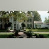 The exterior of Graceland, surrounded by lush green grass and trees, with a brick walkway leading to the front door.