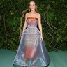 Brie Larson at the Met Gala 2024 red carpet in a shimmering orange Prada gown with a structured skirt.