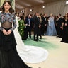 Riley Keough at the Met Gala 2024 red carpet in a dress with a bedazzled top, bare midriff and black flowy skirt.