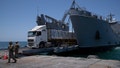 A U.S. Army soldier gestures as trucks loaded with humanitarian aid arrive at the U.S.-built floating pier Trident before reaching the beach on the coast of the Gaza Strip, Tuesday, June 25, 2024.