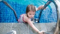 Portrait of a little girl in swimming pool. An active sportive kid standing on ladder in blue water. Top view.