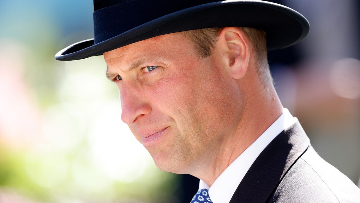 A close-up of Prince William wearing a black suit and a matching top hat.