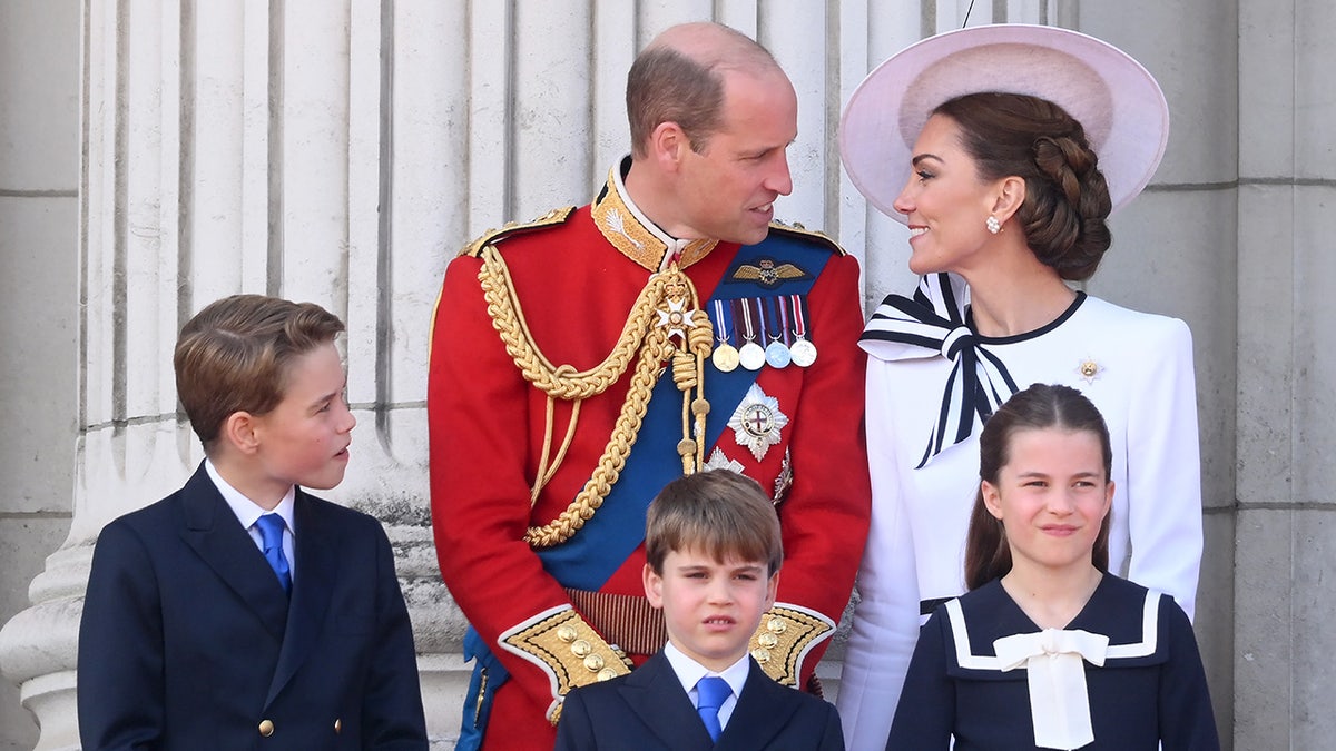 The Prince and Princess of Wales looking at each other adoringly with their three children on the Buckingham Palace balcony
