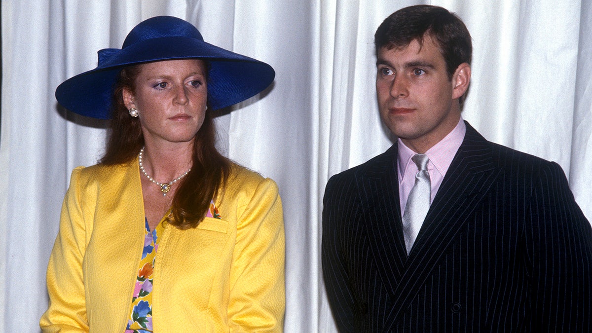 Sarah Ferguson wearing a yellow blazer and blue hat next to Prince Andrew in a black blazer, pink shirt and silver tie.