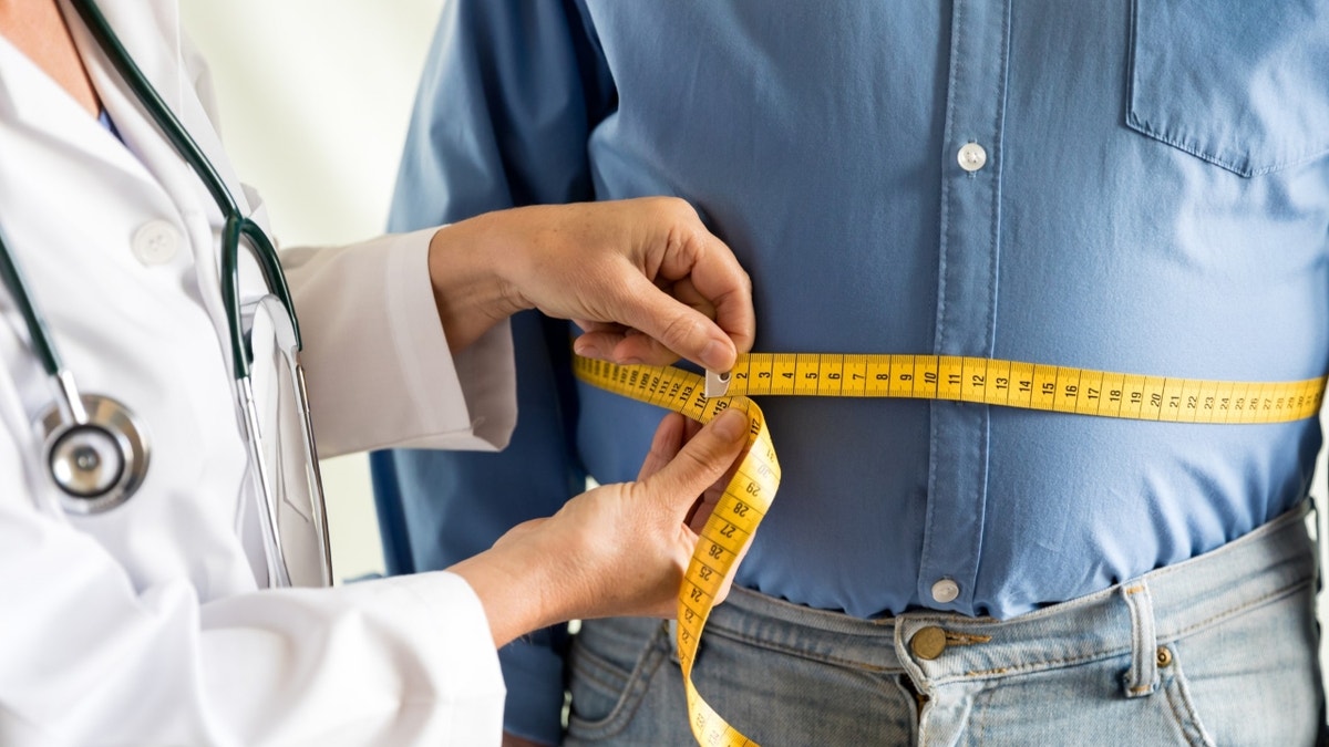 A doctor measures an obese man's waist