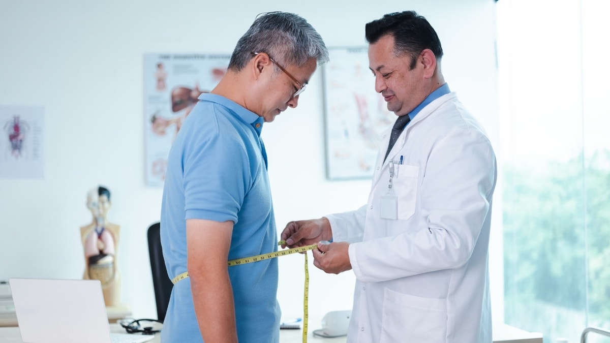 A doctor measures a man's waist
