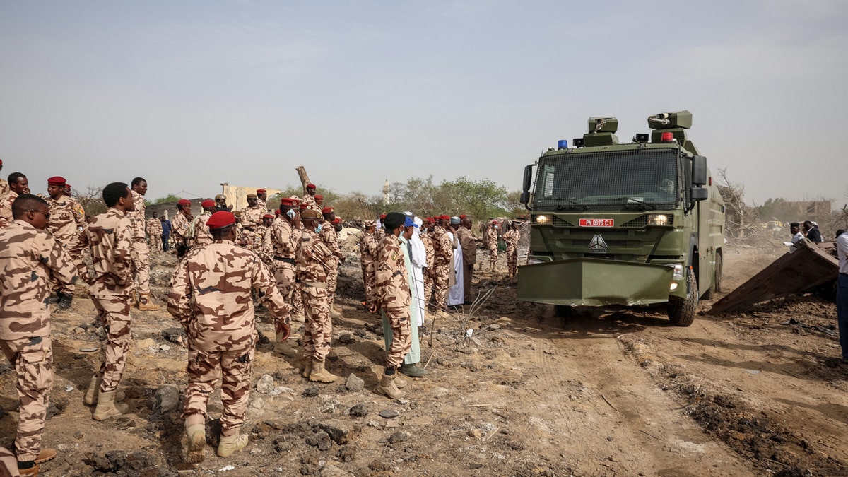 Members of the Chadian security forces dressed in camo fatigues look on as a large, green armored vehicle drives at the scene of the fire at a ammunition depot in N'Djamena on June 19, 2024.