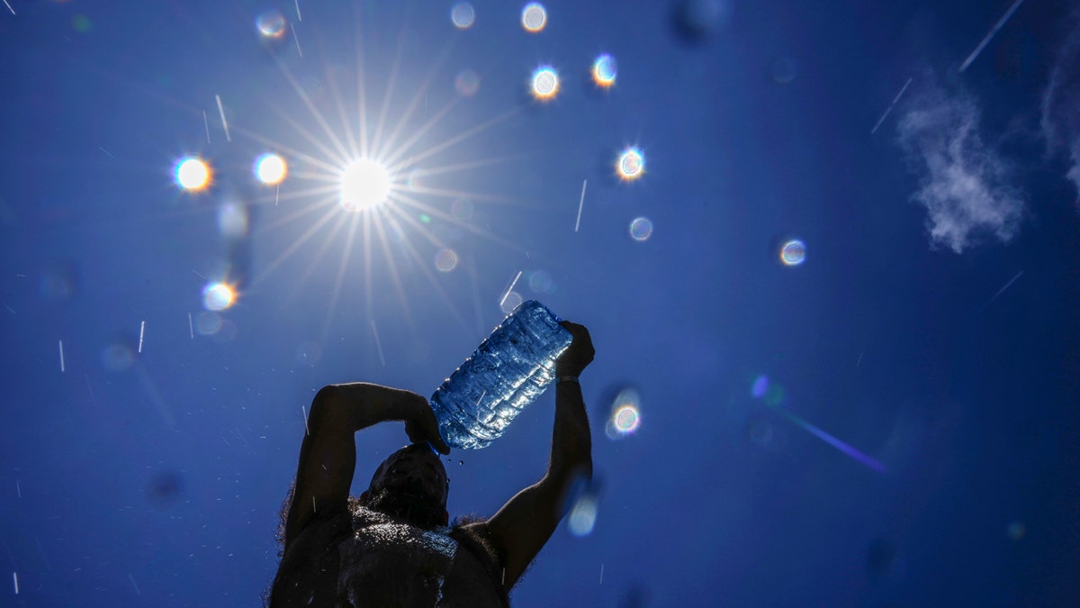 A man pours water onto his head underneath the shining sun to try to keep cool.