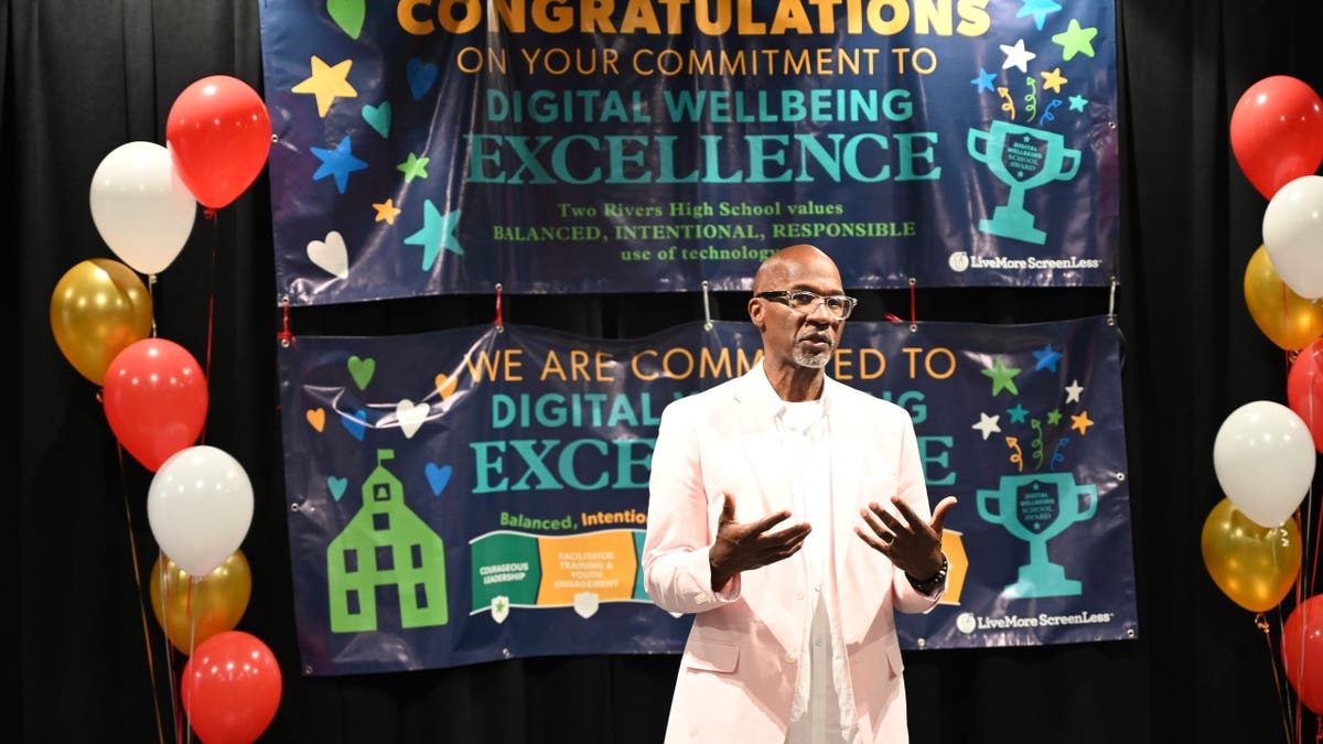 a man speaks in front of a crowd with a congratulations banner behind him