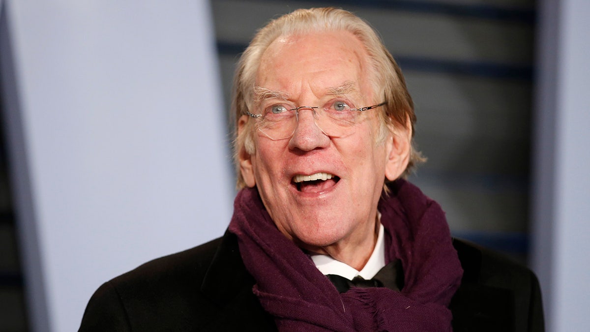 Donald Sutherland sports purple scarf and black coat at Oscars party.