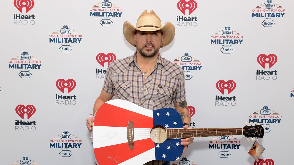 jason aldean posing on a red carpet with an american flag guitar