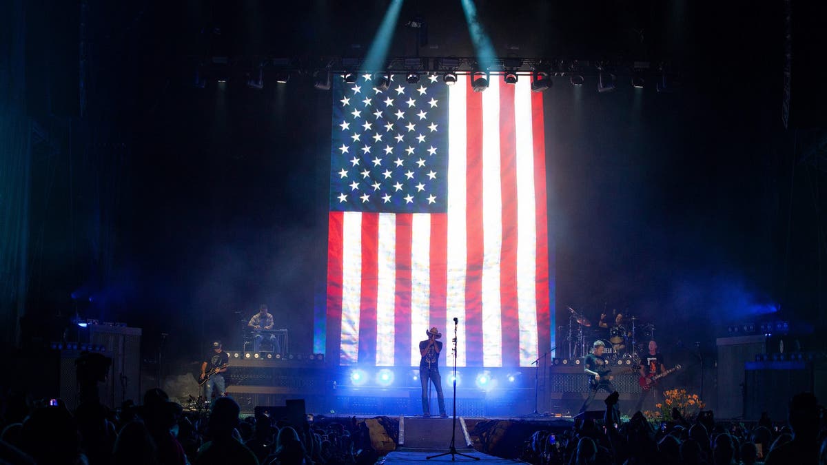 jason aldean performing in front of a giant american flag at concert