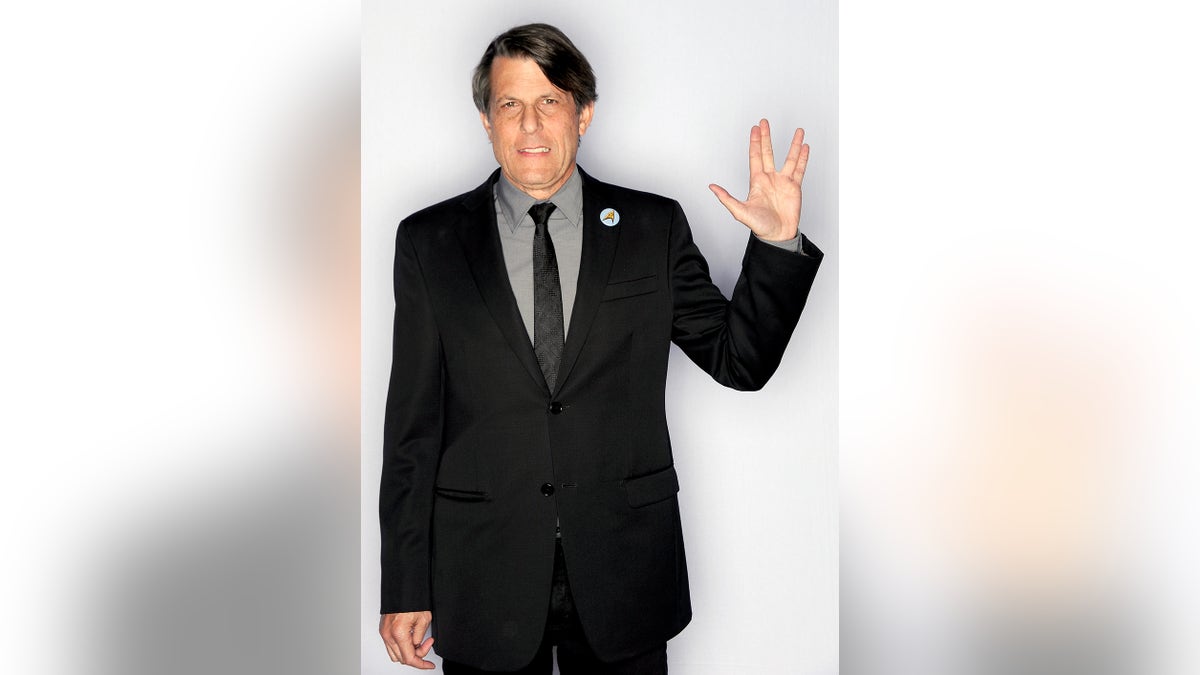 Adam Nimoy doing a Spock sign in a black suit.