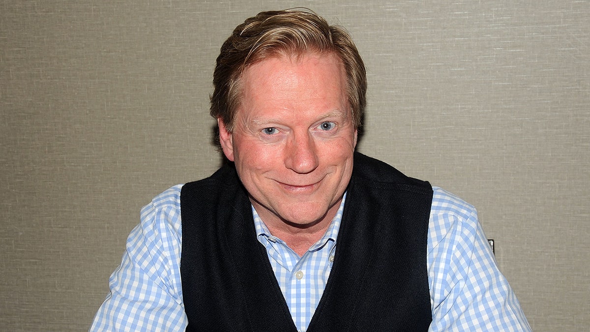 Dean Butler vestindo uma camisa xadrez azul e branca com um colete preto.