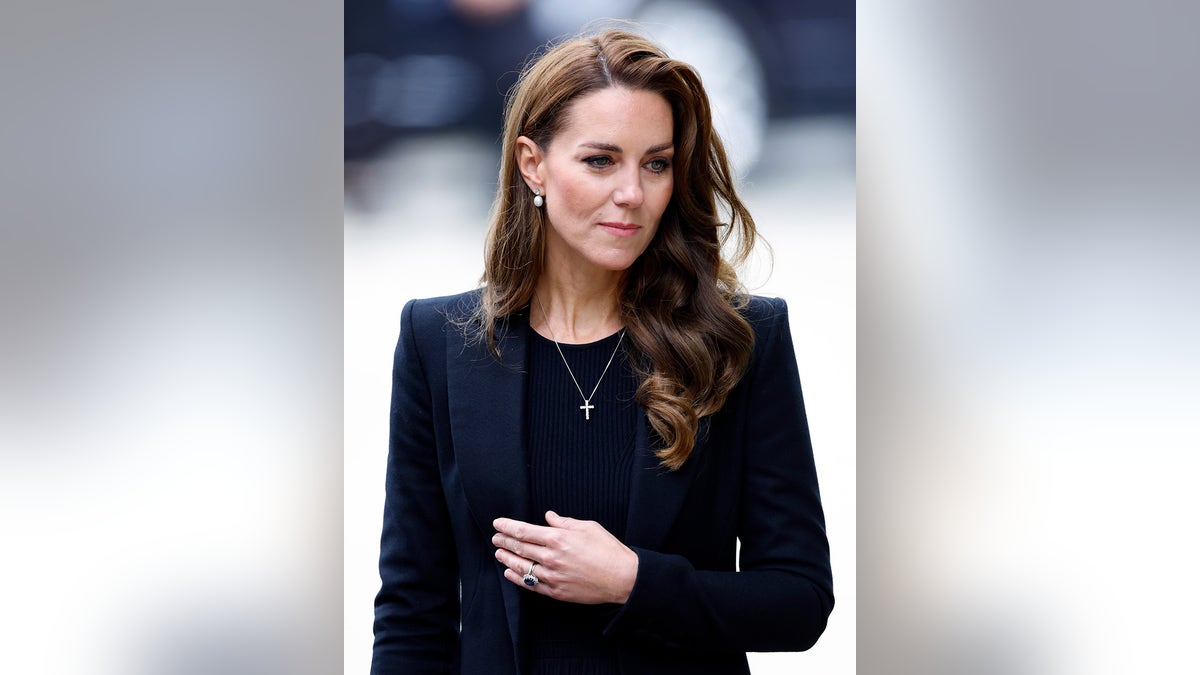 Kate Middleton wearing a navy suit and blazer with a golden cross necklace