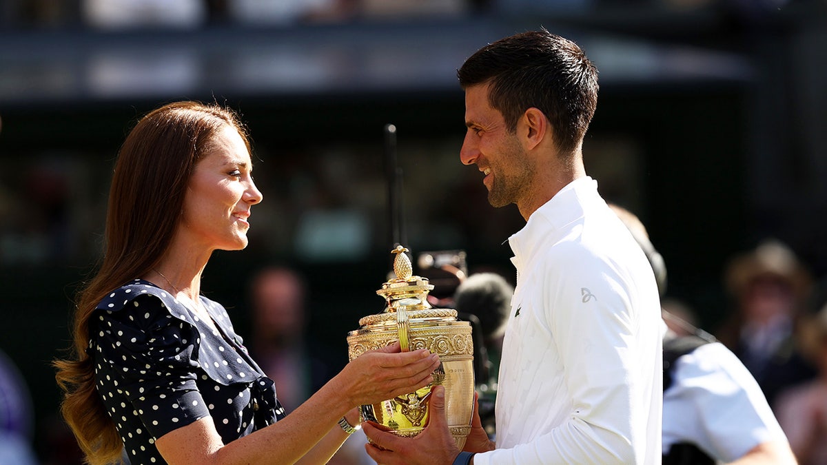 Kate Middleton wearing a black and white polka dot dress handing a trophy to a tennis player.