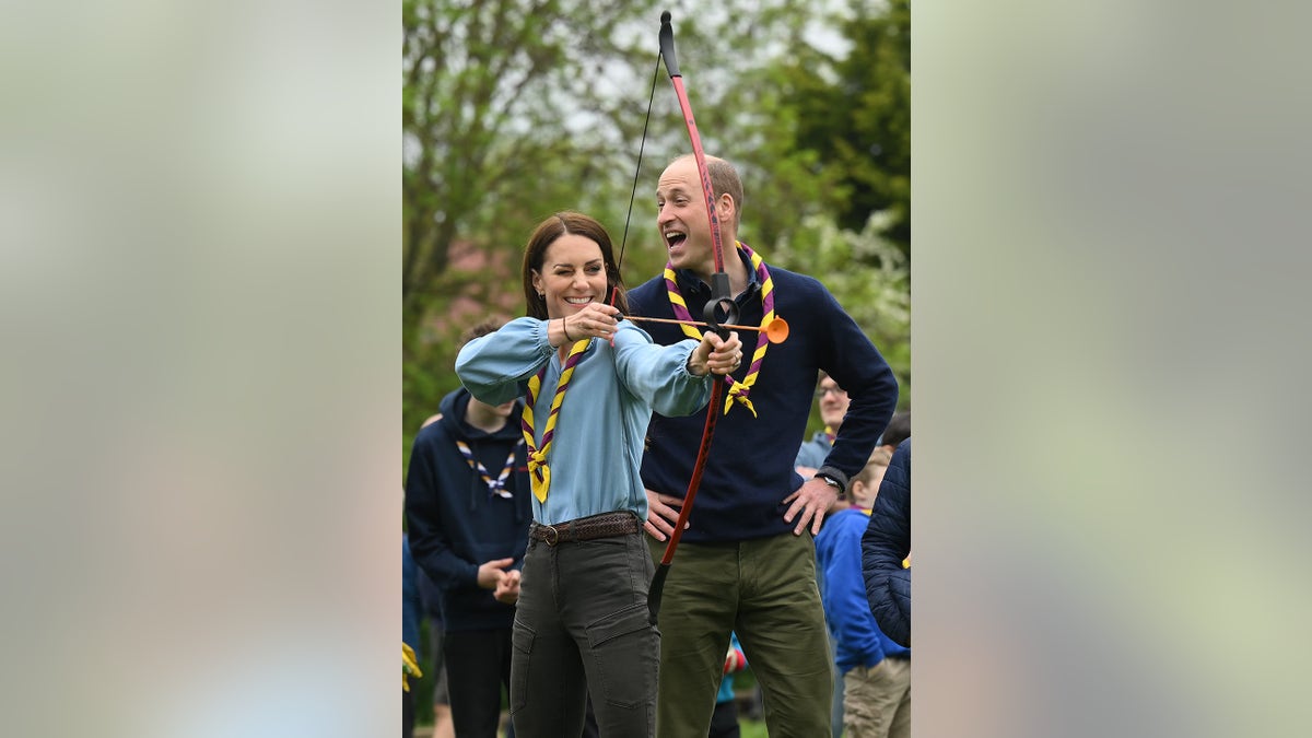 Kate Middleton atirando arco e flecha enquanto o príncipe William a anima