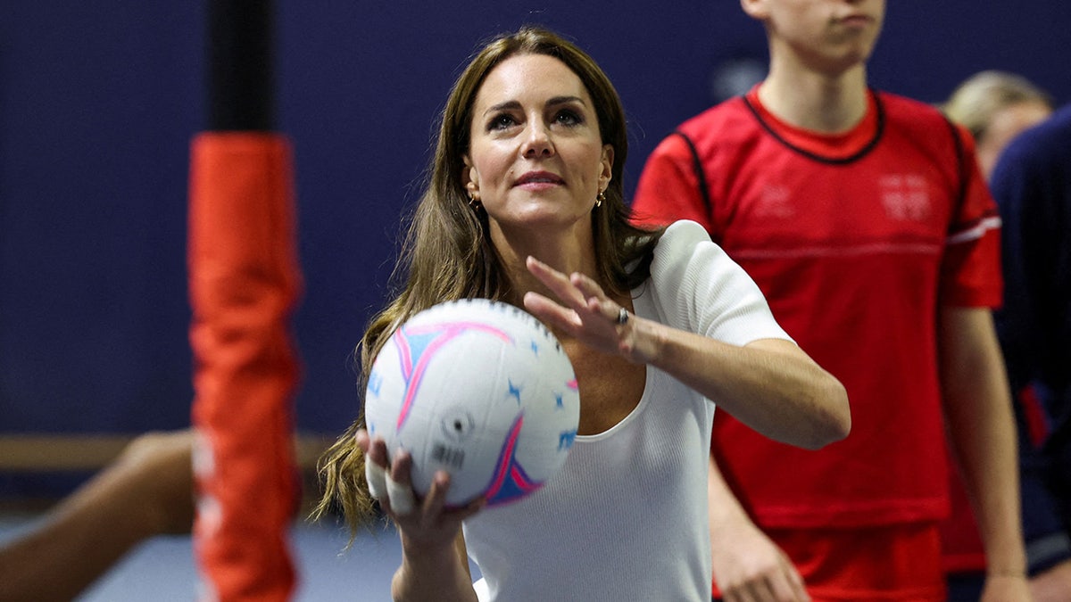 Kate Middleton holding volleyball while playing in a white t-shirt.
