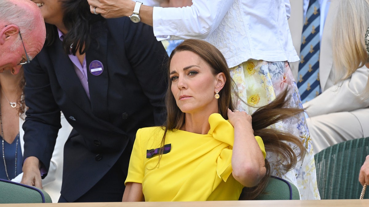 Kate Middleton jogando o cabelo para o lado usando um vestido amarelo brilhante.