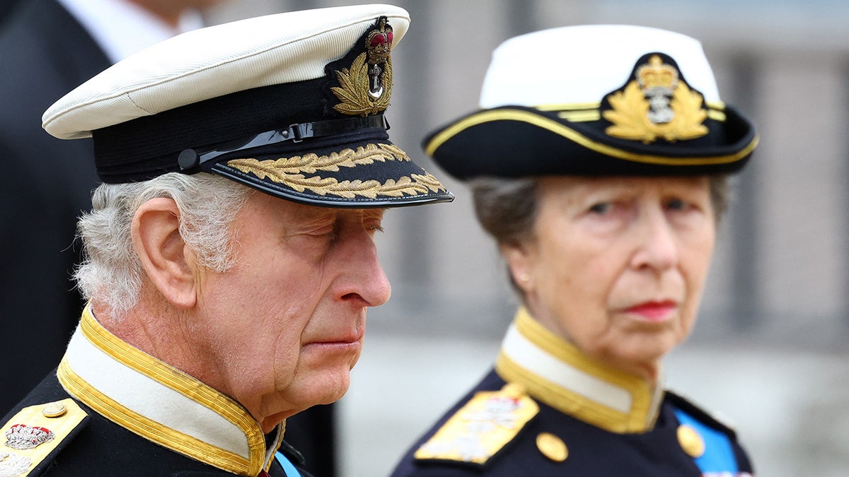 Princess Anne looking at King Charles who has his eyes closed.