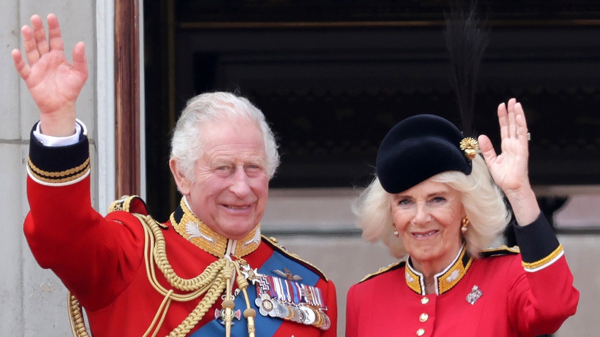 King Charles and Queen Camilla waving in matching red suits from the palace balcony