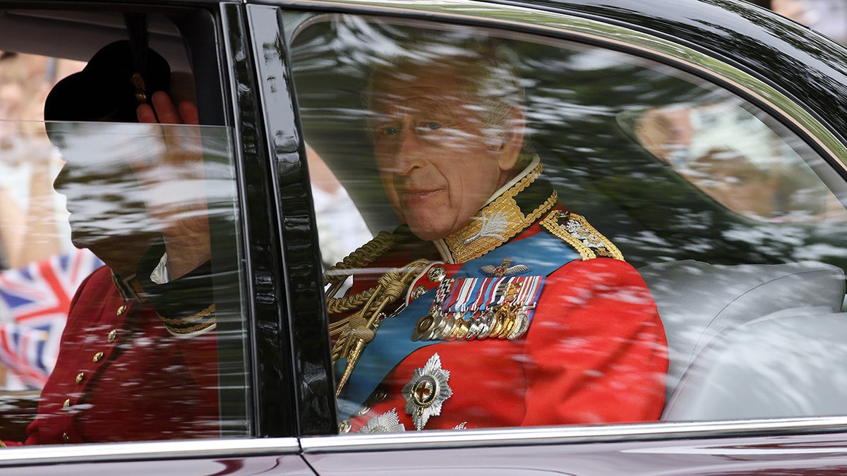 King Charles inside a car wearing a red uniform