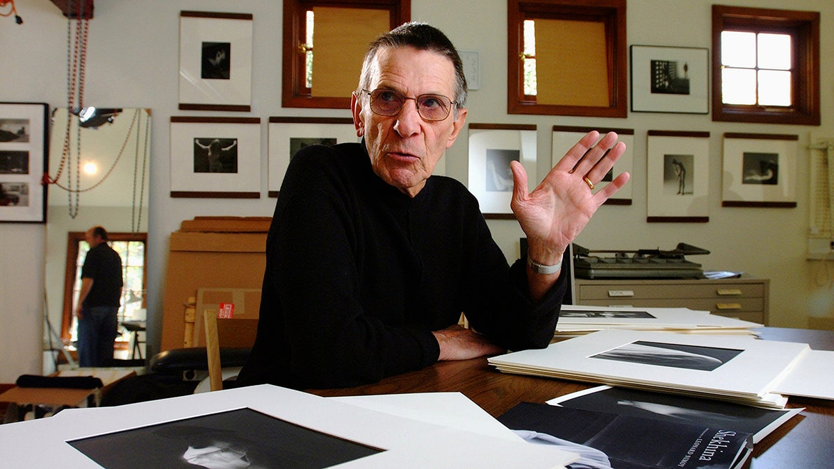 Leonard Nimoy in front of a stack of photographs.